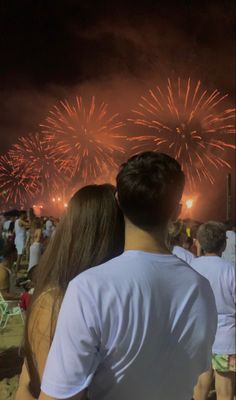 two people watching fireworks on the beach at night with their backs turned to the camera