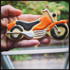 a hand holding a decorated cookie shaped like a motorbike with orange and black accents