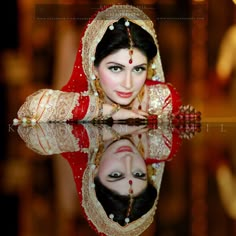 a woman in a red and gold bridal outfit is reflected in the water with her reflection