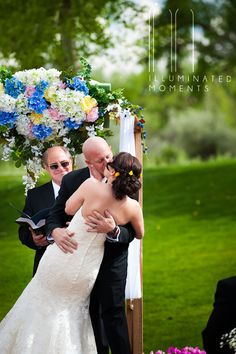 a bride and groom kissing under an arch at their outdoor wedding ceremony in the park