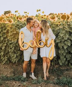 a man, woman and child standing in front of a sunflower field with the word baby spelled out