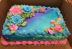 a blue and pink cake with flowers on it in a cardboard box, ready to be eaten