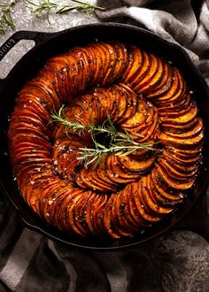 baked sweet potatoes in a cast iron skillet with rosemary sprigs on top