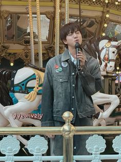 a man standing in front of a merry go round with a microphone on his hand