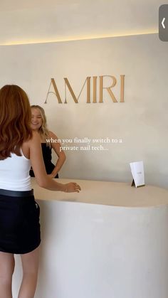 two women are standing at the counter in front of an amri sign