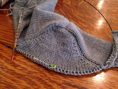 a close up of a knitted object on a wooden table with knitting needles in it