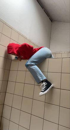 a person in red shirt and blue jeans standing on tiled floor next to white wall