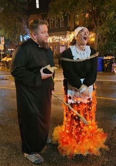 two people dressed in costumes standing next to each other on the street at night time