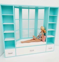 a barbie doll sitting on top of a blue book shelf next to a white wall