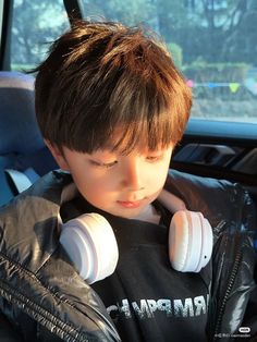 a young boy sitting in the back seat of a car with headphones around his neck