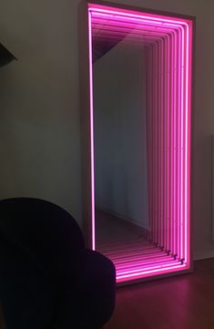 a large mirror with pink lights on it in front of a white wall and black chair