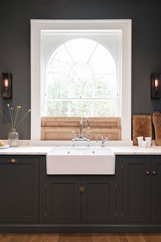 a white kitchen sink sitting under a window next to a wooden counter top and cabinets