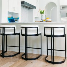 three stools in front of a kitchen island with white counter tops and cabinets,