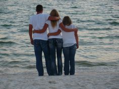 three people standing on the beach with their arms around each other