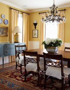 a dining room with yellow walls and white chairs in front of a table that has flowers on it