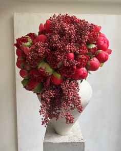 a white vase filled with red flowers on top of a table next to a wall