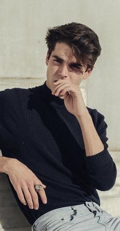 a man sitting on top of a white bench next to a cement wall with his hand under his chin