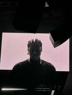 a man with dreadlocks standing in front of a large screen