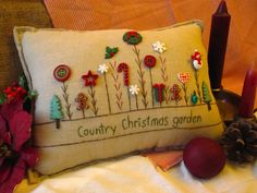 an embroidered pillow with christmas decorations on it next to a candle and some pine cones