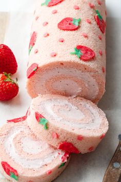 strawberry roll cake with frosting and strawberries on the wrapper next to it