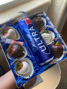 a can of soda and some chocolate covered strawberries in a box on a table