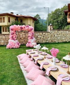 a table set up with pink and white decorations for a birthday party in front of a stone wall