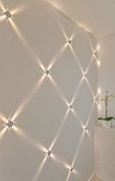 a white wall with some lights on it and a vase in front of the wall