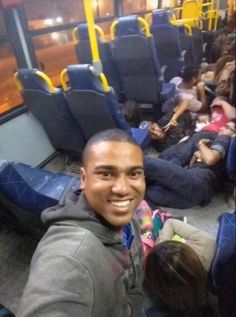 a man sitting on a bus with people sleeping in the seat area next to him