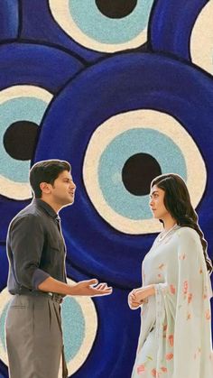 two people standing next to each other in front of an artistic wall with circles on it