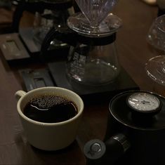 a cup of coffee sitting on top of a wooden table next to a clock and some glasses