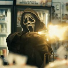 a person in a skeleton mask and hood holding a light up to their face while standing next to a vending machine