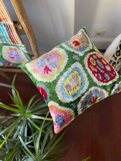 two colorful pillows sitting on top of a wooden chair next to a potted plant