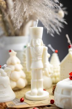 some white candles are on a table with christmas decorations in front of them and a small tree