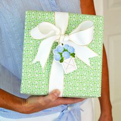 a woman is holding a green gift box with blue flowers on it and white ribbon