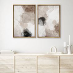 two paintings on the wall above a dresser in a living room with white walls and wooden furniture