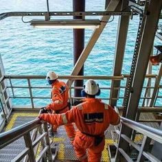 two people in orange suits climbing up stairs to the ocean from a boat on a body of water