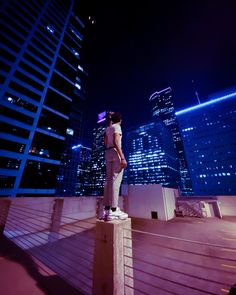 a man standing on top of a roof next to tall buildings in the city at night