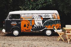 an orange and black van parked on top of a dirt field next to trees,