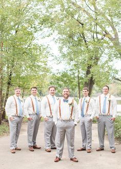 a group of men standing next to each other in front of trees and bushes with ties on