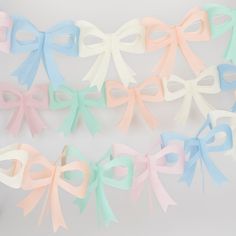 several pastel colored bows are hanging on a white wall in the shape of bowes