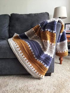 a crocheted blanket sitting on top of a gray couch next to a lamp