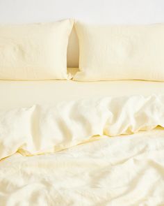 an unmade bed with two pillows on top of it and white sheets in the background