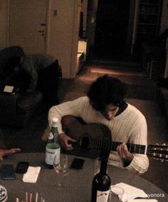 two people sitting at a table playing guitar and wine bottles on the table next to them