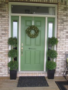 a green front door with two potted plants