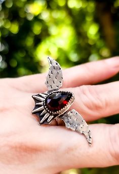 This unique garnet bat wing ring captures the essence of gothic elegance with its intricate design and striking appearance.   The centerpiece of the ring is a captivating garnet, known for its rich, deep red color and lustrous shine. Ring design size 1.8 inches wide �× .9 inches long. Size 7. Ready to ship. Wing Ring, Gothic Elegance, Bat Wing, Deep Red Color, Statement Ring Silver, Intricate Design, Ring Sterling Silver, Bat Wings, Deep Red