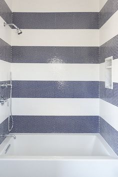 a bathroom with blue and white stripes on the walls, shower head, and bathtub