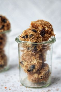 two jars filled with granola and raisins on top of a white table