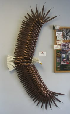 an eagle sculpture hanging on the wall next to a bulletin board with pictures and magnets