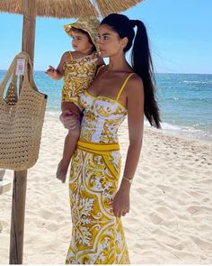 a woman holding a baby under an umbrella on the beach