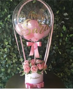 a pink balloon with flowers and balloons in it sitting on top of a wooden table